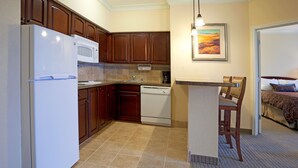 A compact kitchen with a refrigerator, microwave, and dishwasher. There's a small island with a chair, and a painting on the wall.