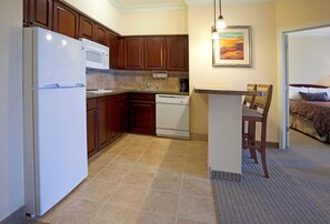 Cocina compacta equipada con refrigerador, microondas y lavavajillas. Hay una pequeña isla con un asiento y un cuadro en la pared.