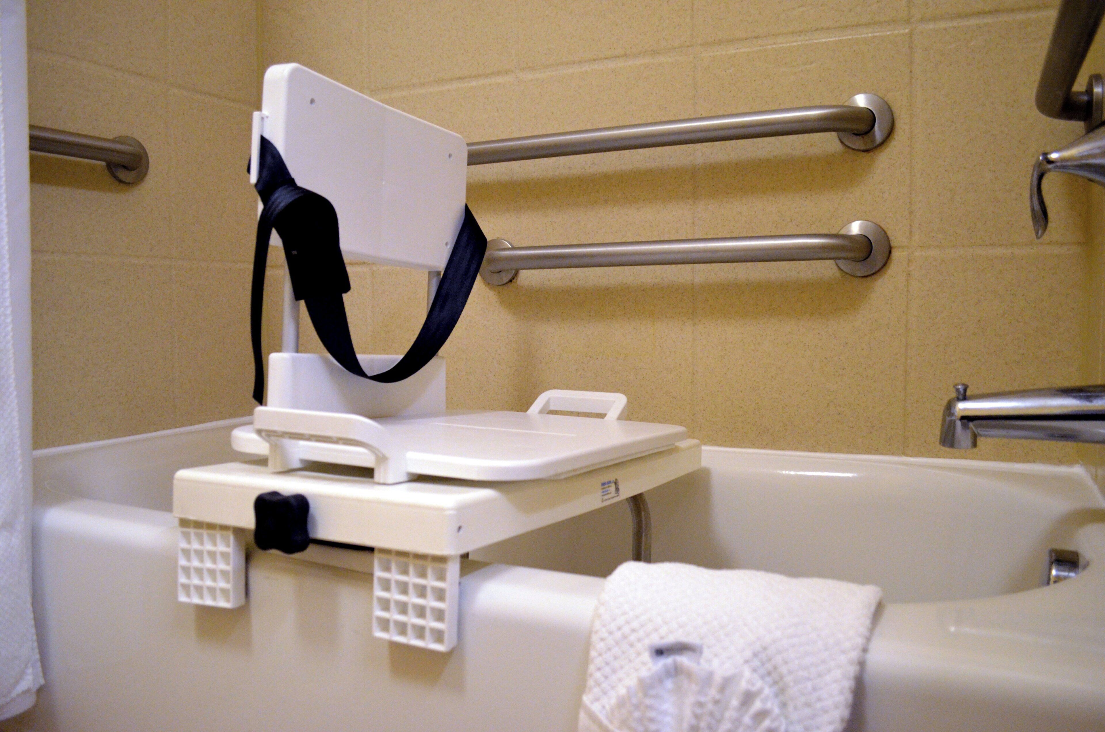 Une salle de bain avec une baignoire, des barres d’appui et une serviette blanche.