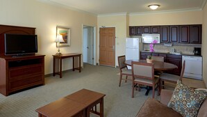 A living room with a TV, wooden furniture, a dining table, and a kitchen area with cabinets and appliances.