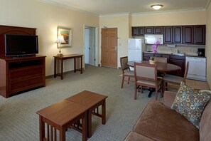 Una sala de estar con televisor, muebles de madera, una mesa de comedor y una zona de cocina con armarios y electrodomésticos.