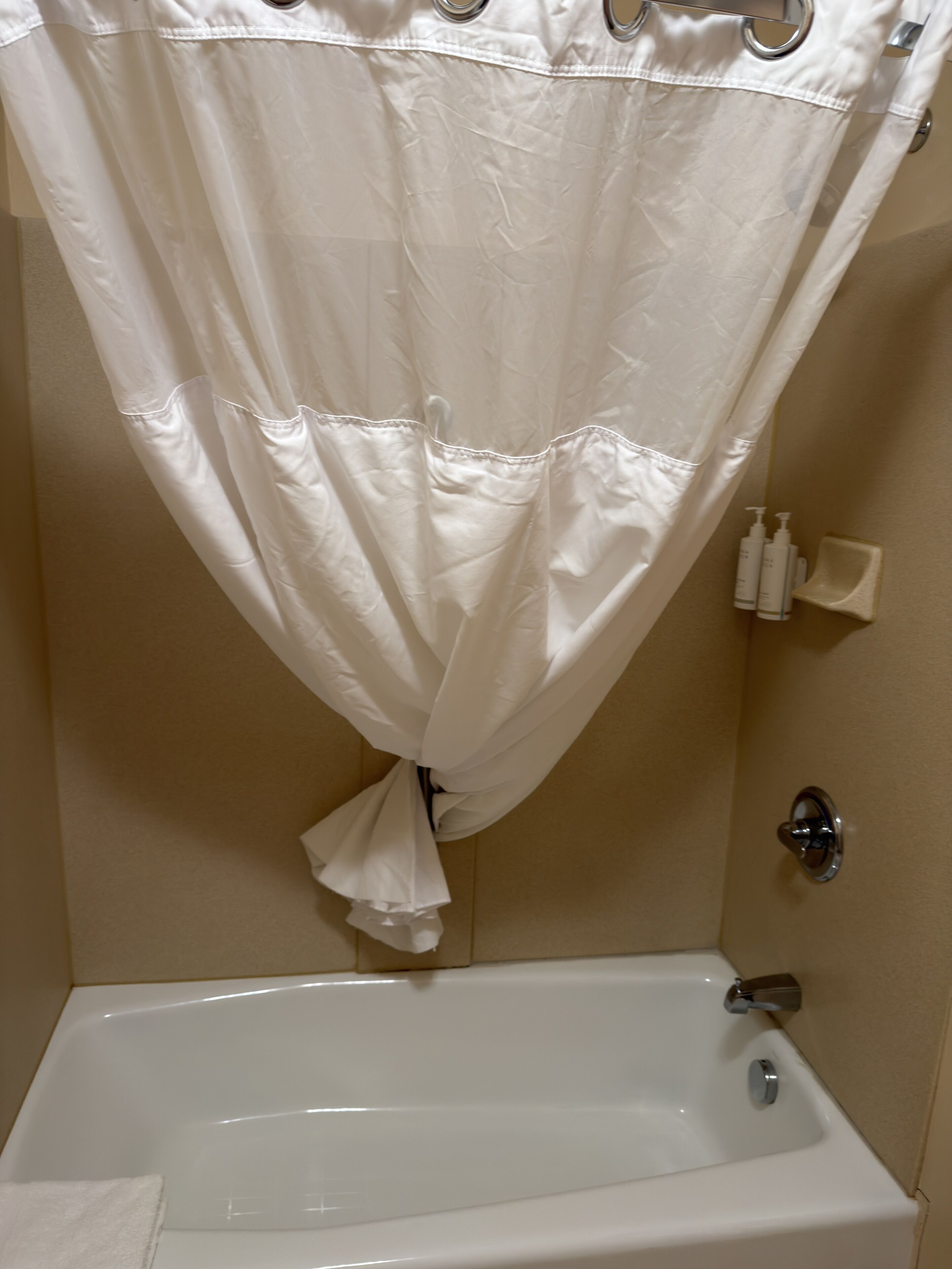 Une salle de bain avec une baignoire blanche, un rideau de douche et des articles de toilette rangés sur une étagère.