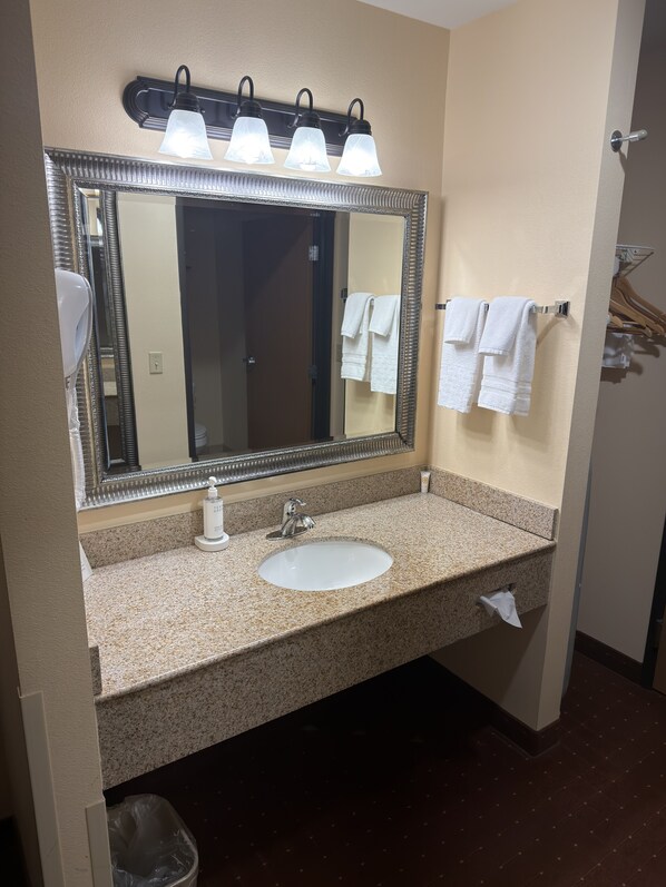 A bathroom with a large mirror, a sink, and three towel hooks. - Americas Best Value Inn St. Robert (St. Robert)