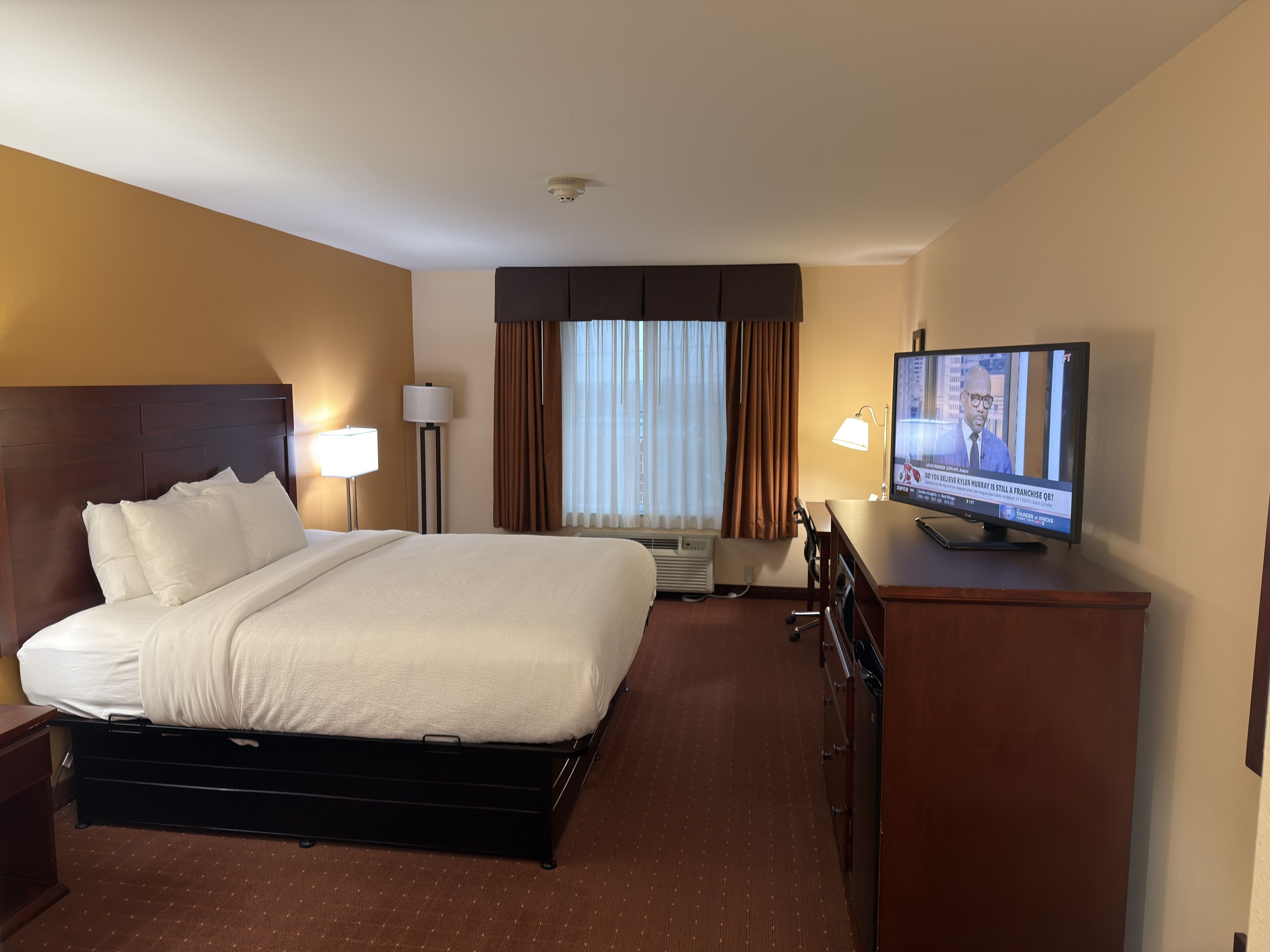 A hotel room with a bed, bedside lamps, a television, a desk, and a dresser.