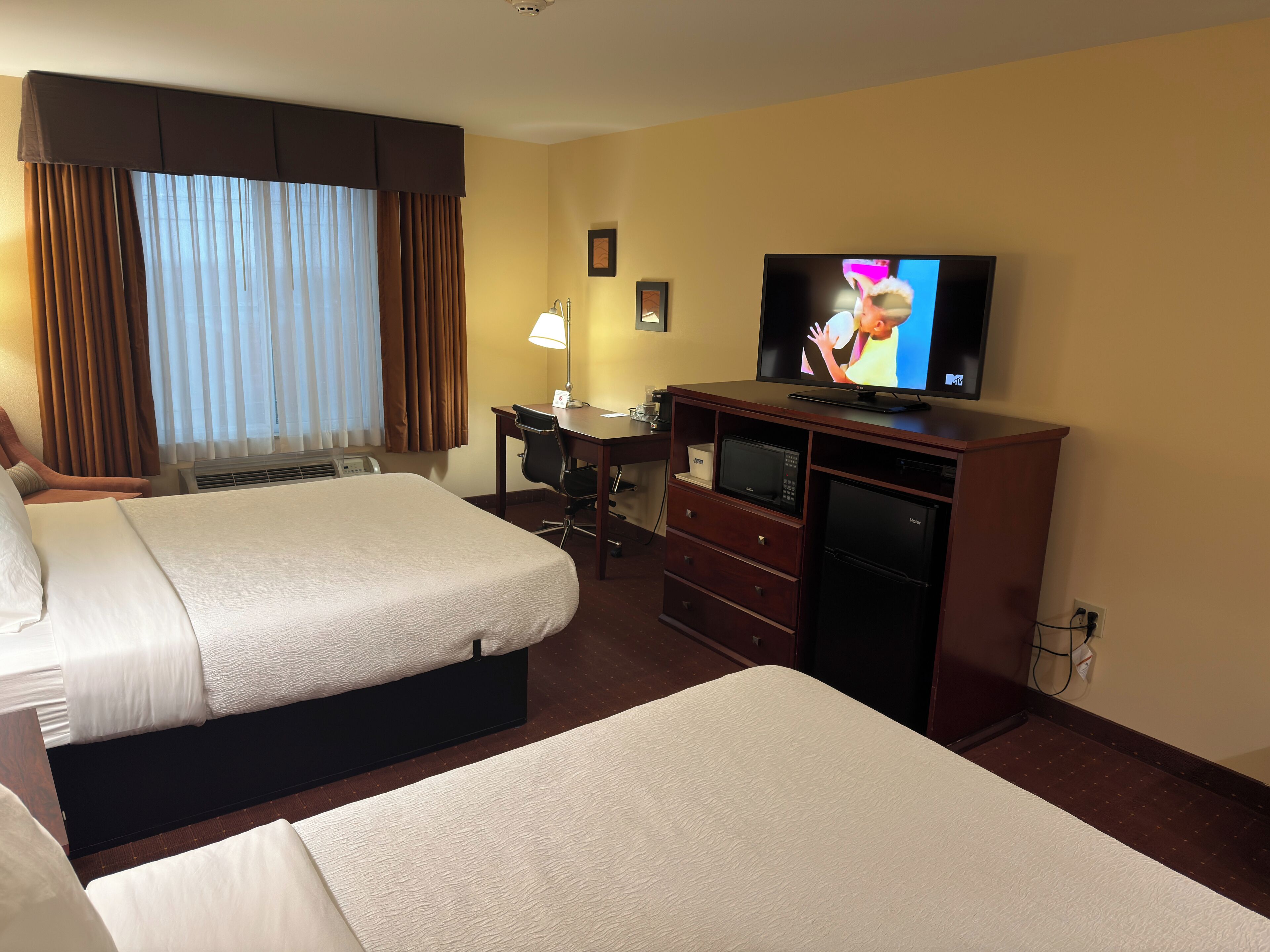 Une chambre d’hôtel avec deux lits, un bureau avec une lampe, une télévision et un mini-bar.