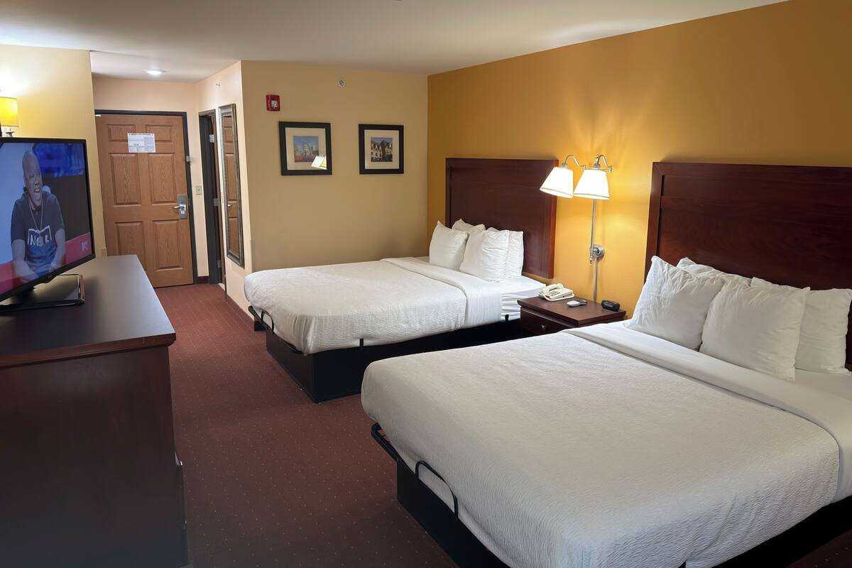 A hotel room with two beds, a TV, a desk, and a lamp.