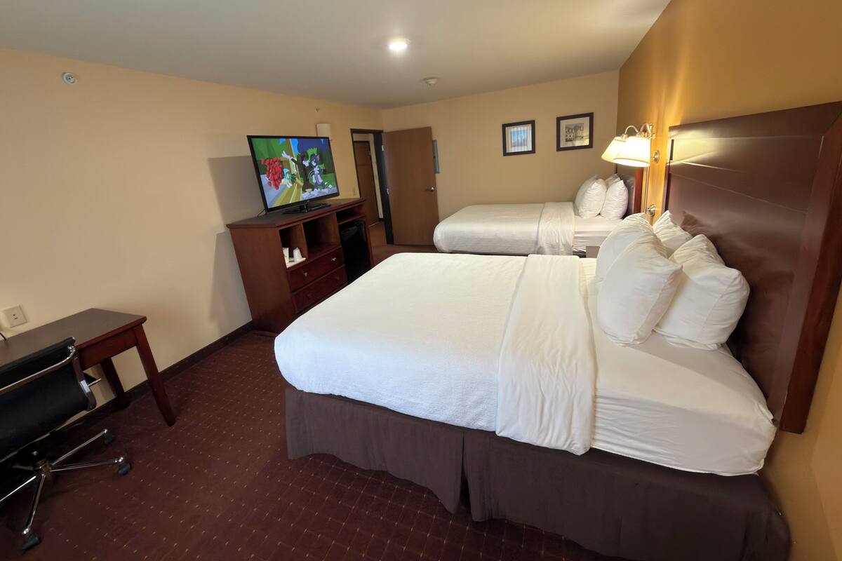 A hotel room with two beds, a desk, a TV, and a lamp.