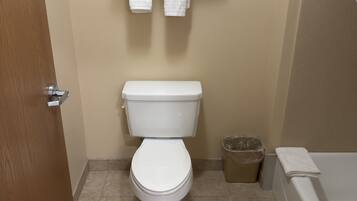 Un baño con inodoro, perchero con toallas, cubo de basura y bañera.