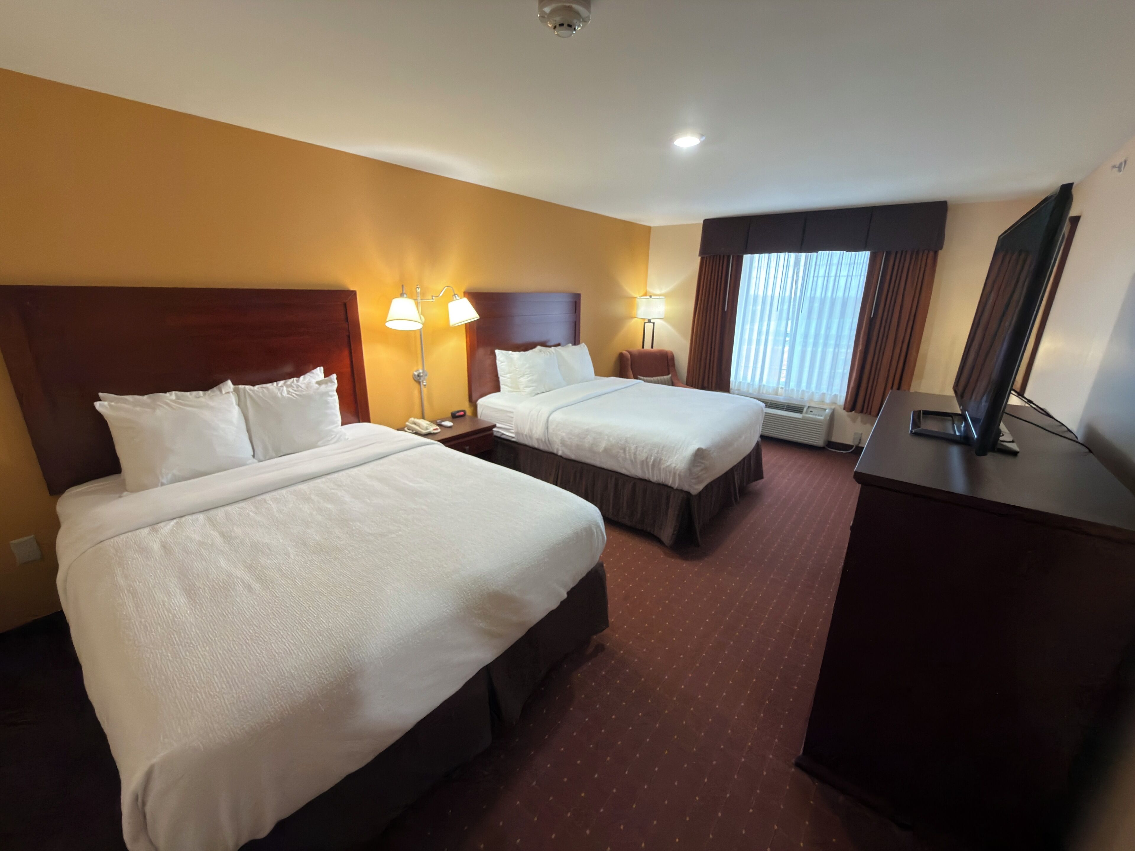 Een hotelkamer met twee bedden, een bureau, een flatscreen-tv en een raam met gordijnen.