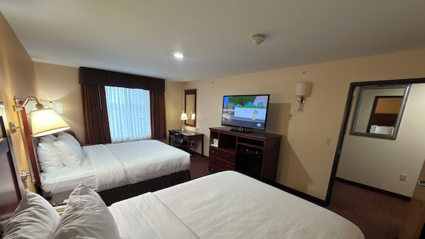 A hotel room with two beds, a desk, a television, and a mirror.