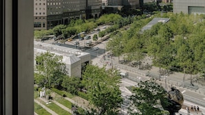 Une vue urbaine avec des gratte-ciel modernes, une place centrale ornée d’une sculpture et un ciel dégagé.