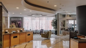 Un hall d’hôtel moderne avec un comptoir d’accueil, un espace salon et de grandes fenêtres.