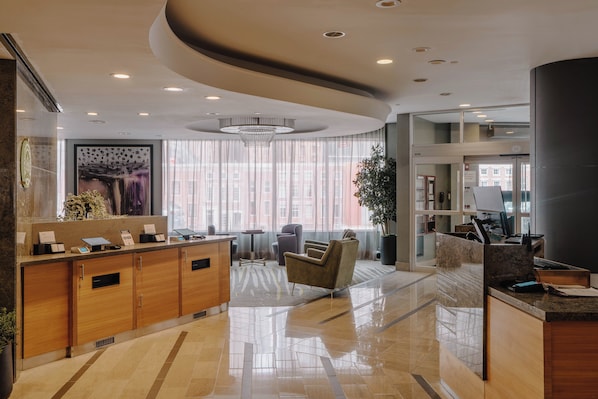 A modern hotel lobby with a reception desk, seating area, and large windows.