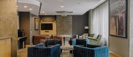 Un moderno vestíbulo de hotel con techo curvo, una mesa redonda central y zonas de estar con sofás tapizados en azul.