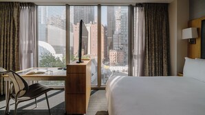 Une chambre d’hôtel avec une grande fenêtre, un bureau avec une chaise, un lit et une lampe.