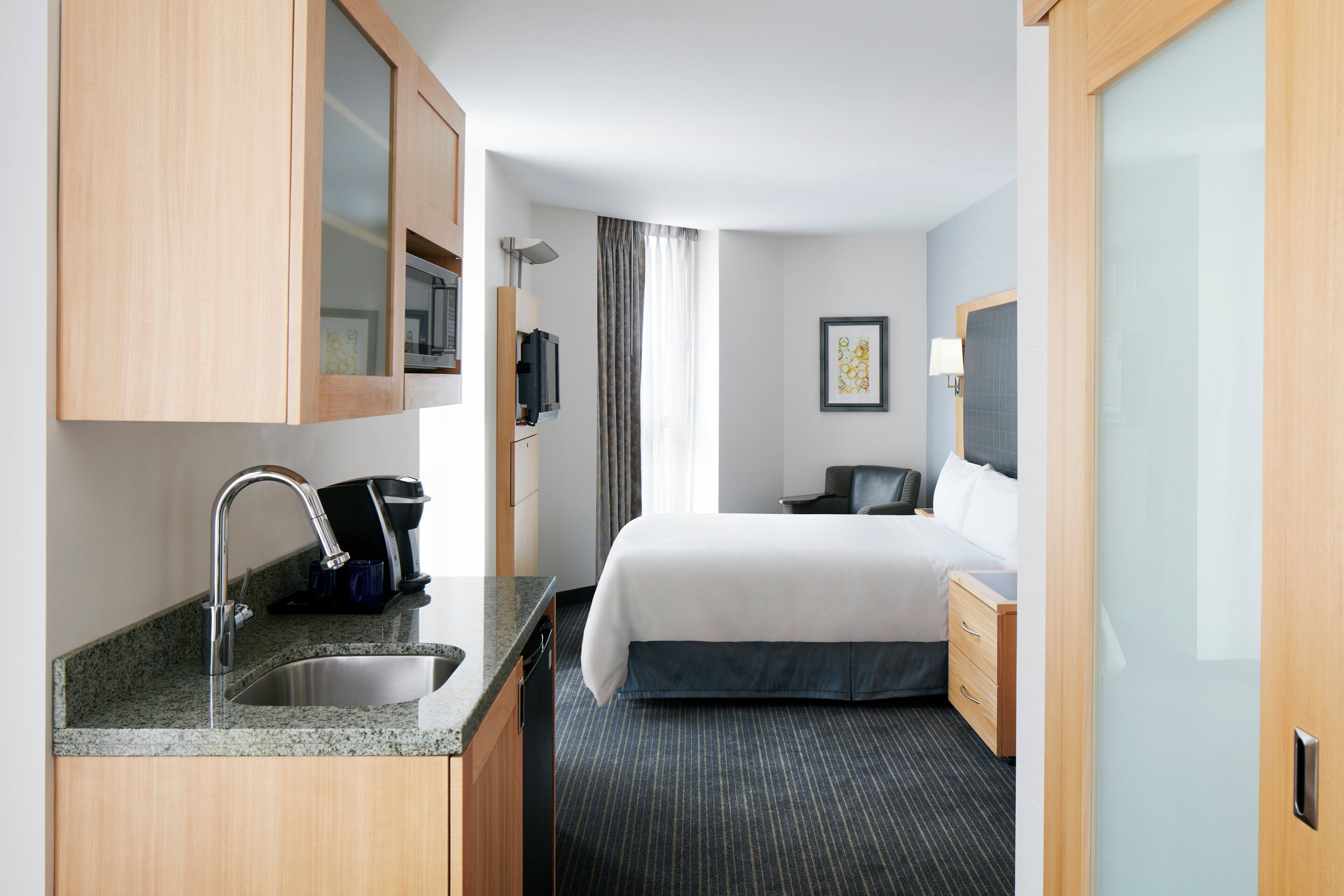 A hotel room with a bed, a desk, a sink, and a television.