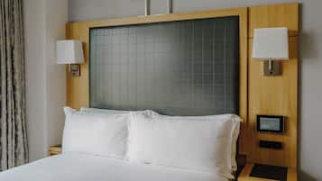 Habitación de hotel con una cama grande, dos lámparas de noche, un panel de control y una ventana con cortinas.