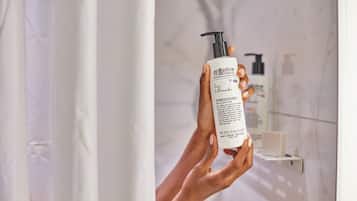 Eine Person hält eine Flasche Bigelow Conditioner in einem Badezimmer mit einer Marmorwand und einem Seifenspender im Hintergrund.