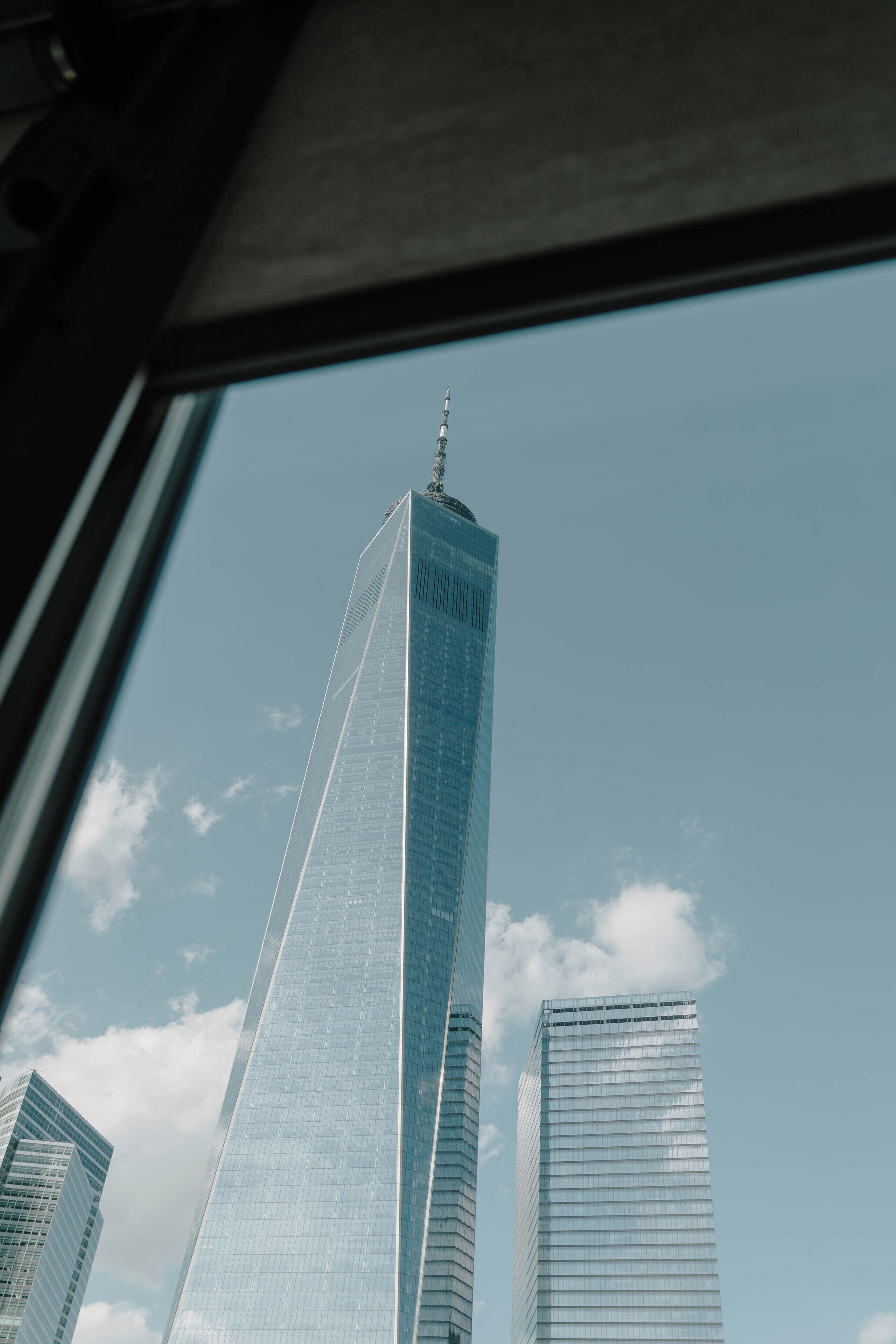 Un rascacielos alto visible a través de una ventana, con otros edificios al fondo.