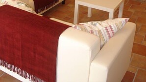Un salon avec un ensemble de canapés blancs, un plaid rouge, une petite table blanche et une cheminée.