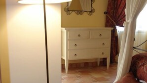 Une chambre d’hôtel avec un canapé blanc, un tapis rouge, une commode blanche, une lampe sur pied et un miroir au mur.