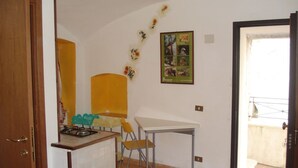 Une petite cuisine avec un réchaud à gaz, une chaise jaune, une table blanche et une affiche encadrée représentant des animaux sauvages accrochée au mur.