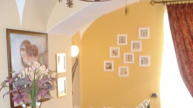 Une pièce avec une commode en bois, un vase rempli de fleurs et un mur orné de tableaux encadrés.
