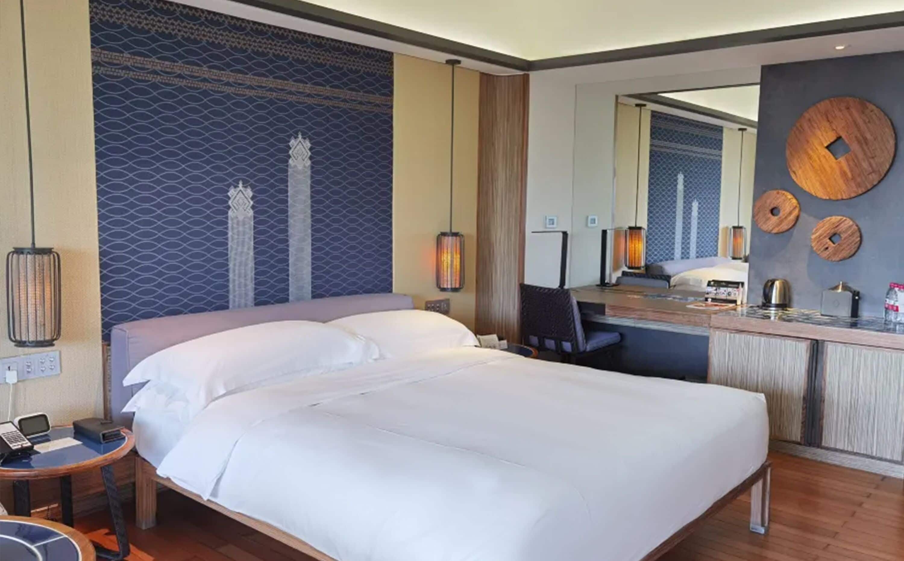 Camera d'albergo con un letto grande, una scrivania con una sedia, un tavolino con un telefono e uno specchio.