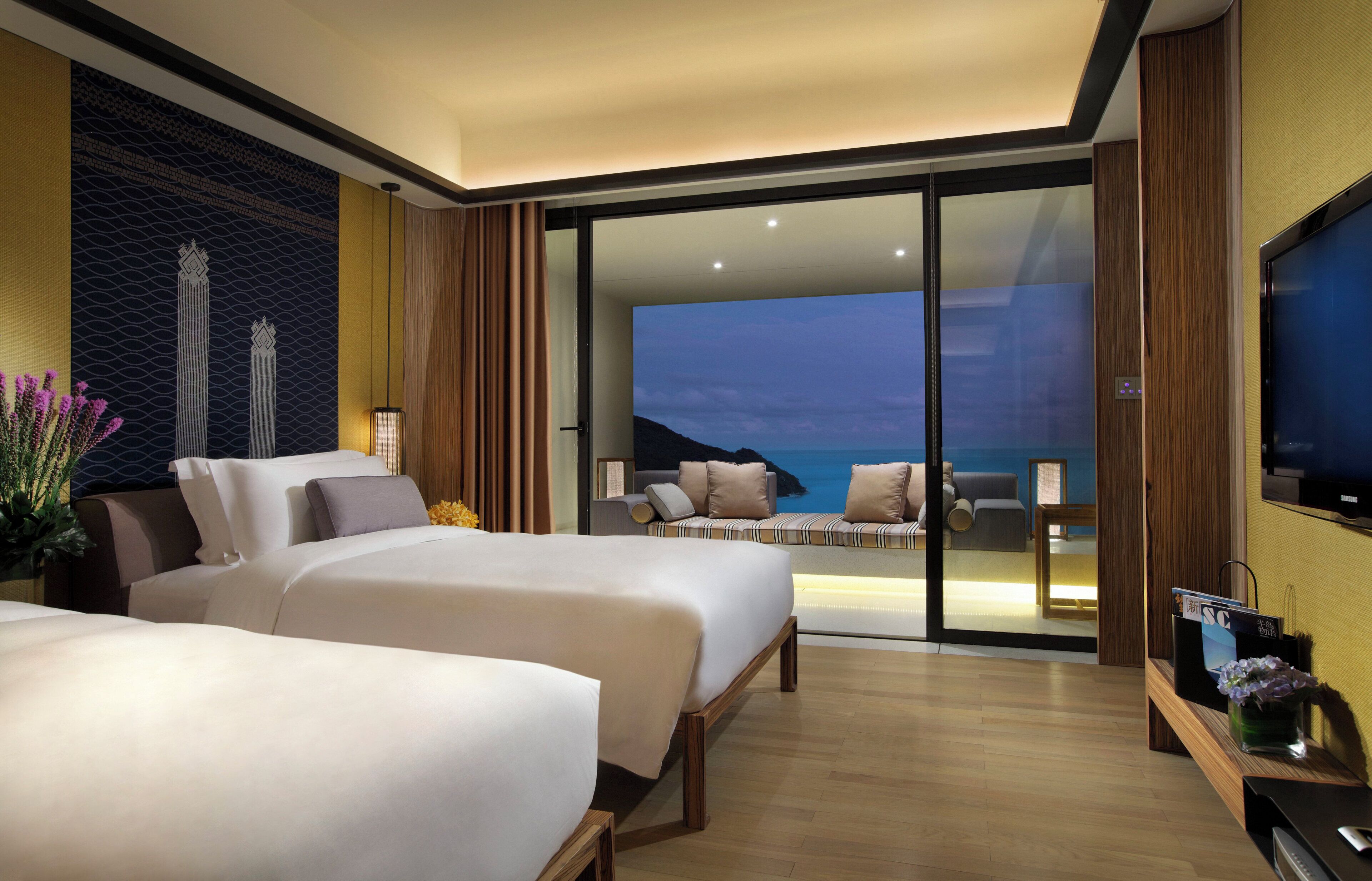 A hotel room with two beds, a television, and a view of the sea.