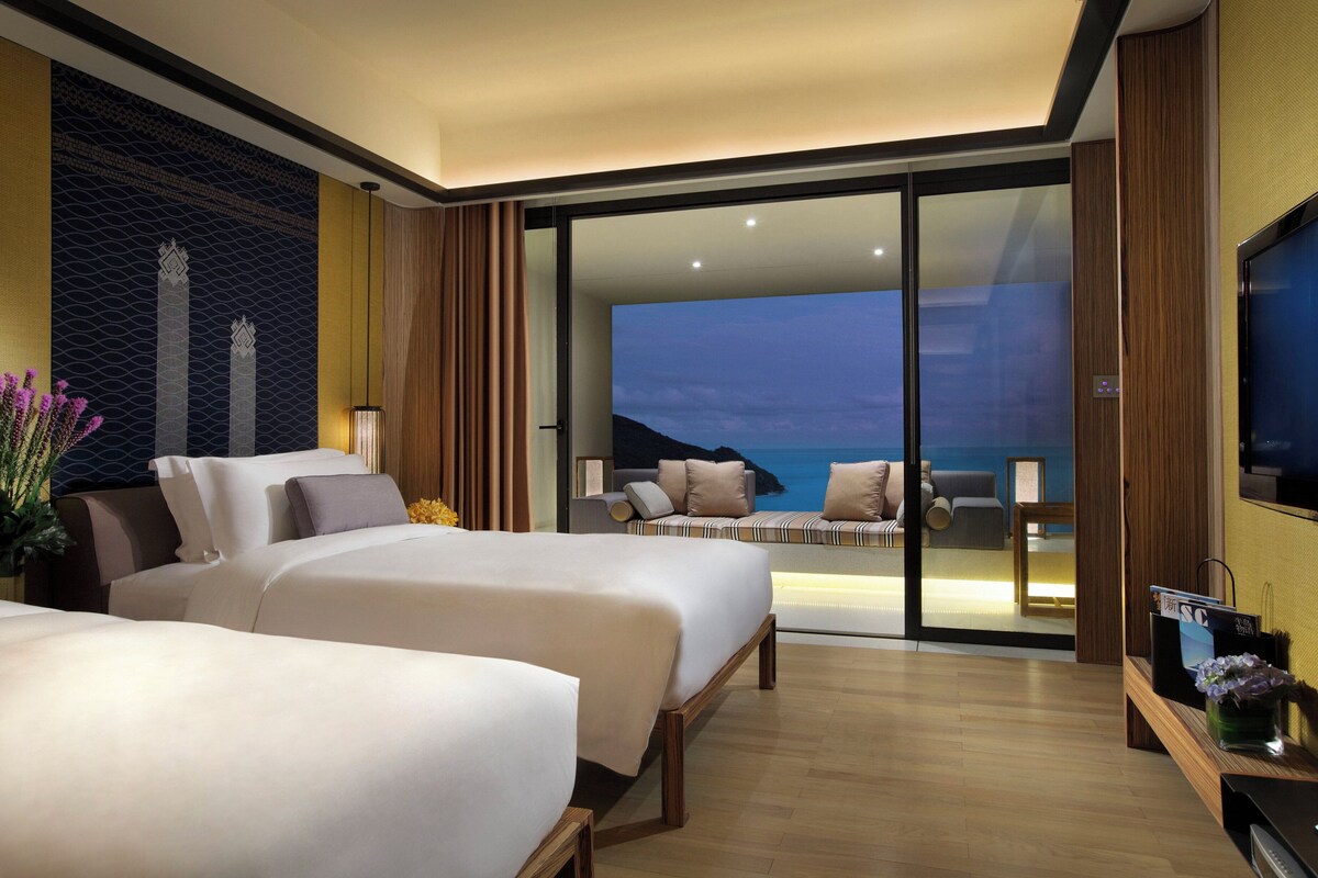 Habitación de hotel con dos camas, televisión y balcón con vista al océano.