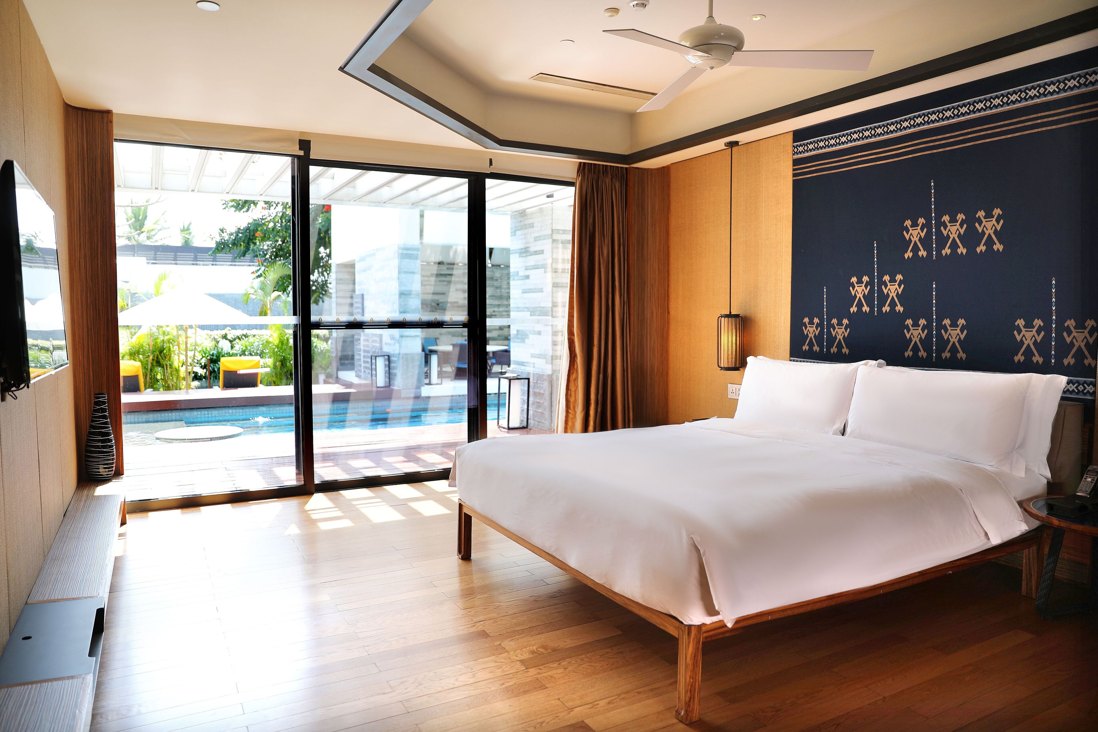 Un'ampia camera da letto con un letto grande, una porta scorrevole in vetro che dà su un balcone con piscina e vista sulla città.