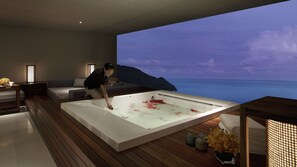 Un spa moderno con una bañera grande, piso de madera y vista al océano.