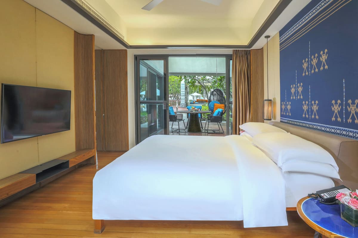 A hotel room with a large bed, a TV, a dining area with outdoor seating, and a decorative wall.