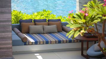 Zona de estar junto a la piscina con un banco acolchado, una mesita pequeña y abundante vegetación.