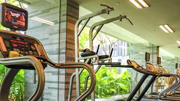 Un gimnasio con cintas de correr y equipo de ejercicio, rodeado de plantas tropicales.
