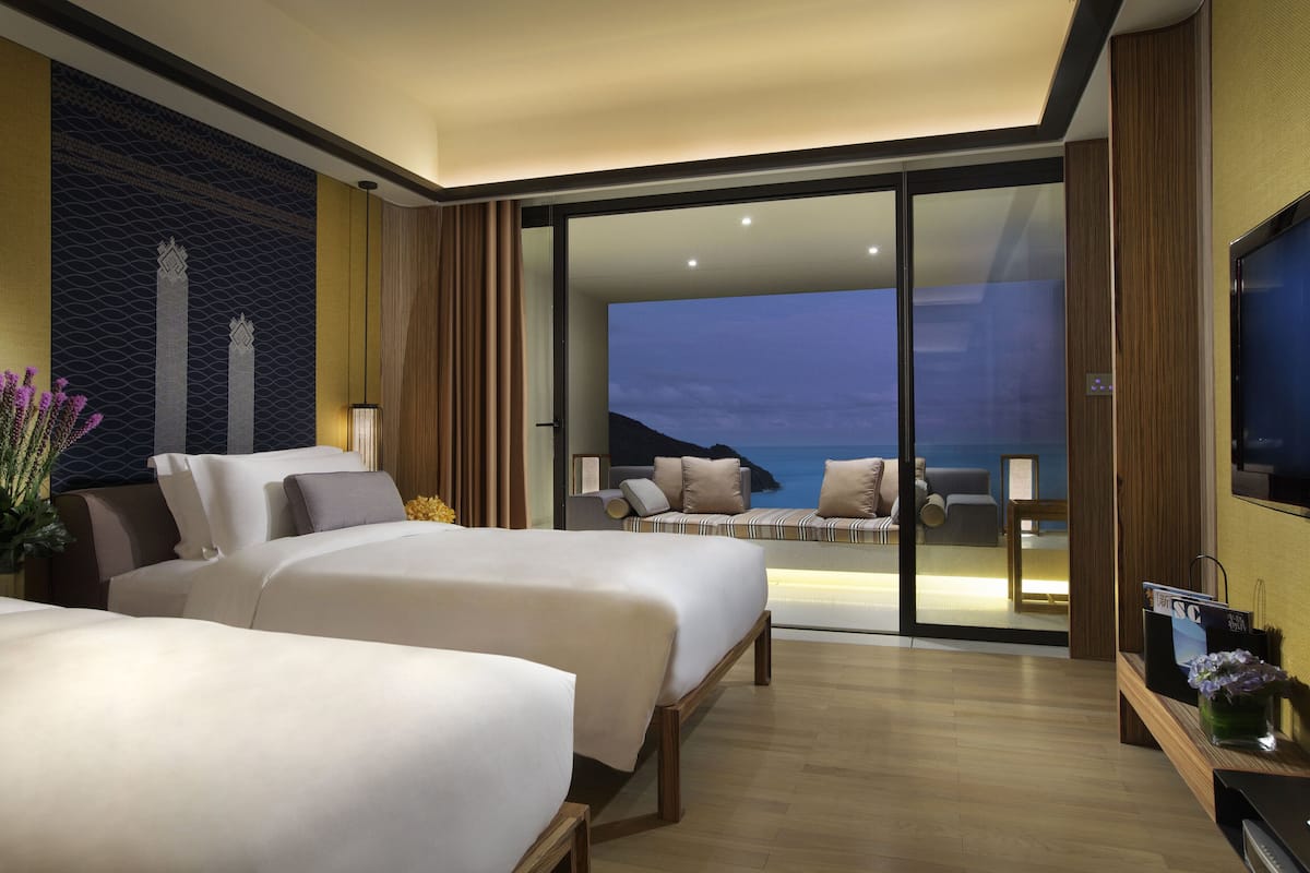 A hotel room with two beds, a TV, and a balcony with a view of the ocean.