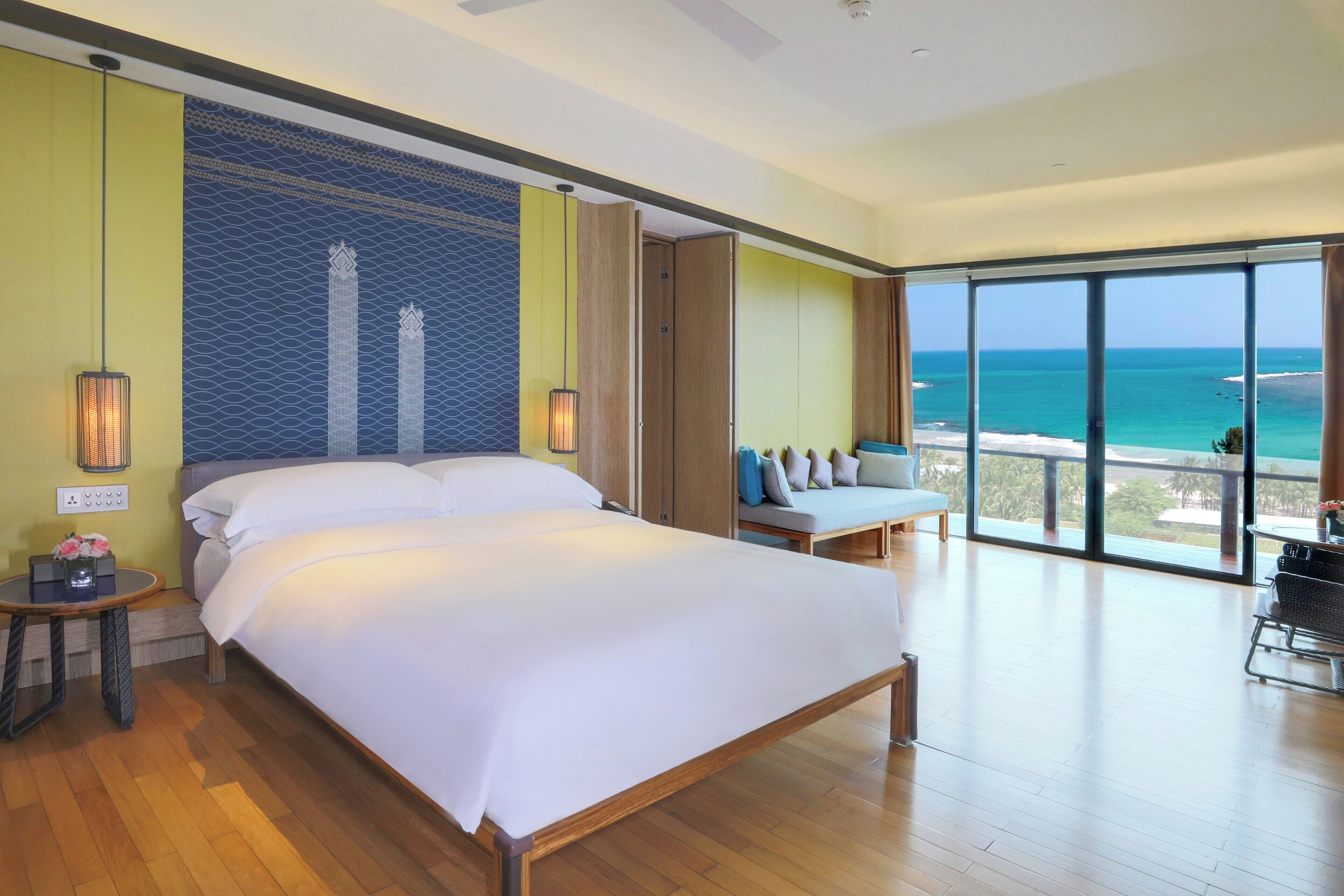 A spacious bedroom with a large bed, a seating area with a view of the ocean, and a balcony with a table and chairs.