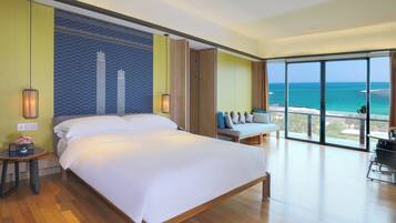 A spacious bedroom with a large bed, a seating area with a view of the ocean, and a balcony with a table and chairs.