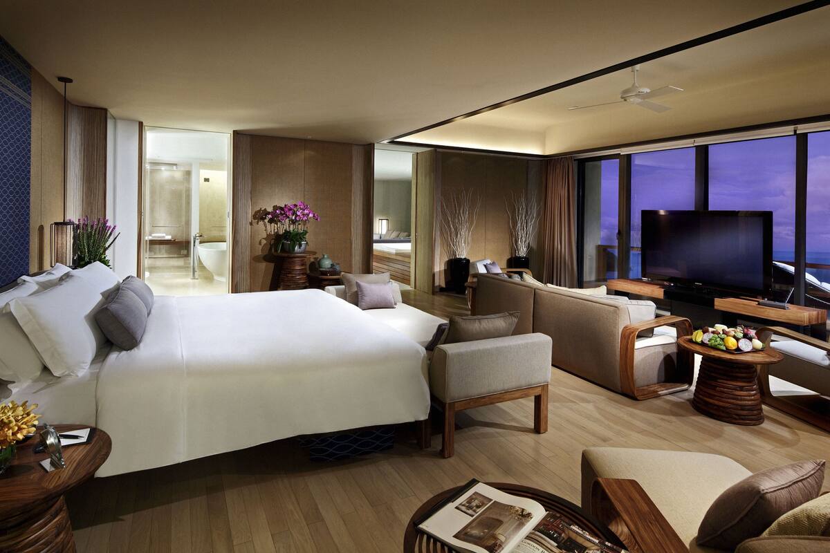 A modern hotel room with a large bed, a sofa, a TV, and a view of the ocean.
