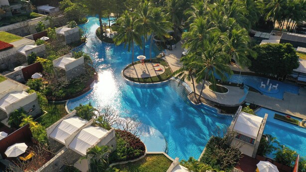 Ett semesterhotell med en central pool omgiven av palmer och solstolar.