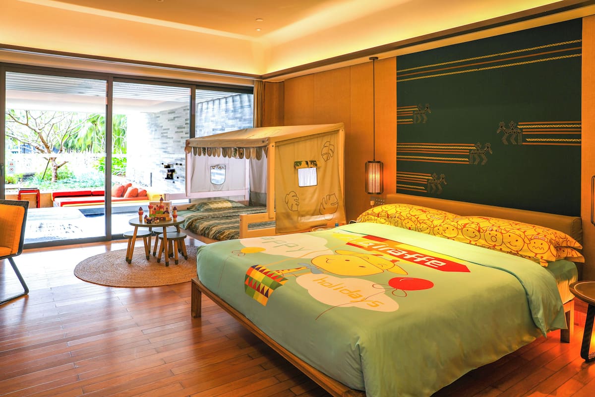 A modern hotel room with a large bed, a small table, a chair, and a view of the outdoors.