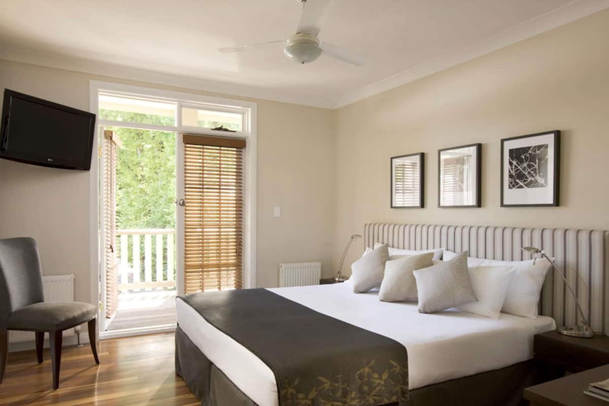 A bedroom with a bed, a chair, a TV, and a balcony with blinds.