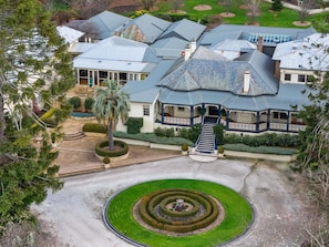 A large estate with a central circular garden, a grand staircase leading to a covered porch, and multiple buildings with varied roof designs. - Peppers Craigieburn (Bowral)