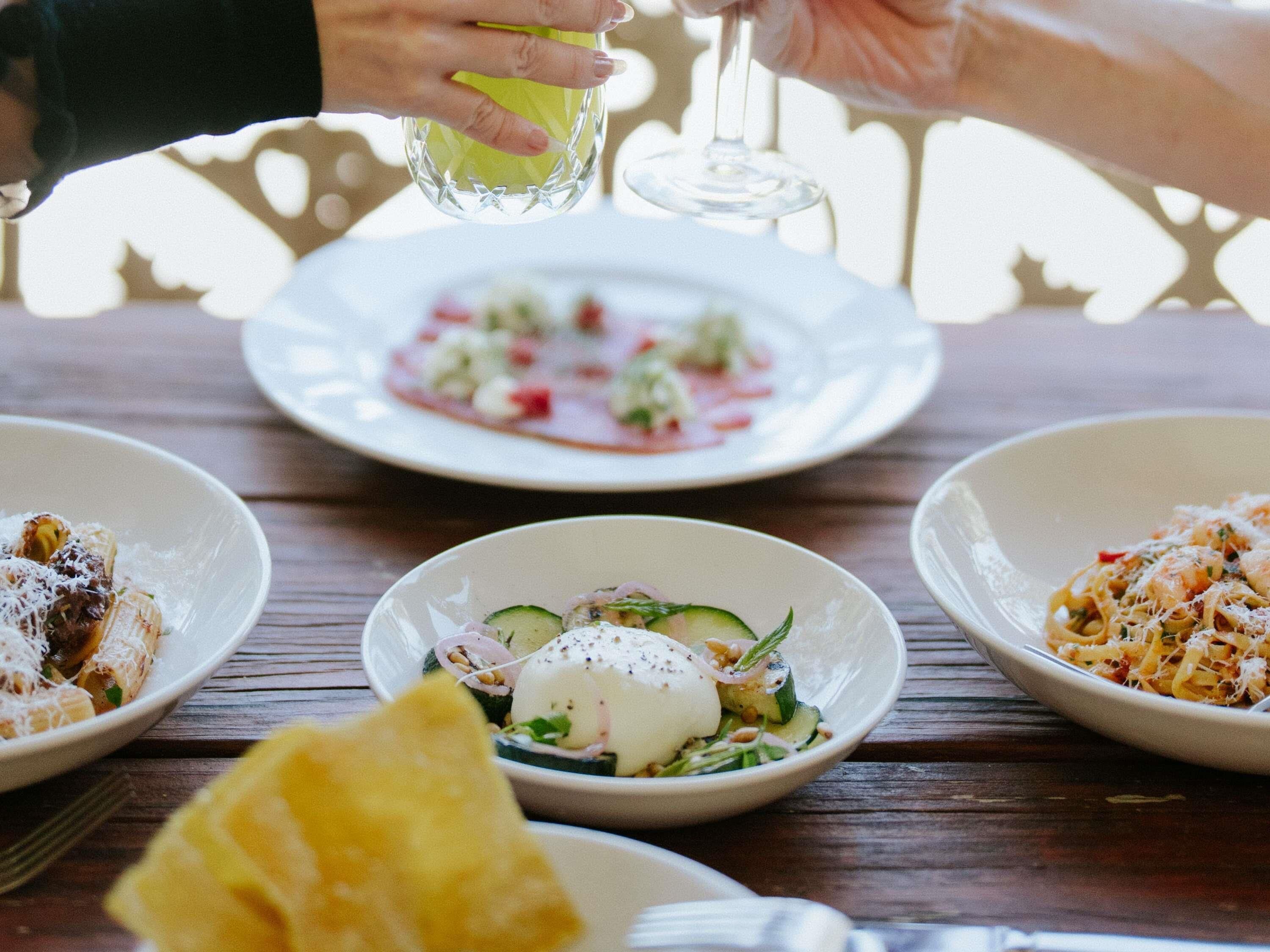 A wooden table with three plates of food, a glass of water, and a glass of wine.