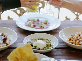 A wooden table with three plates of food, a glass of water, and a glass of wine.