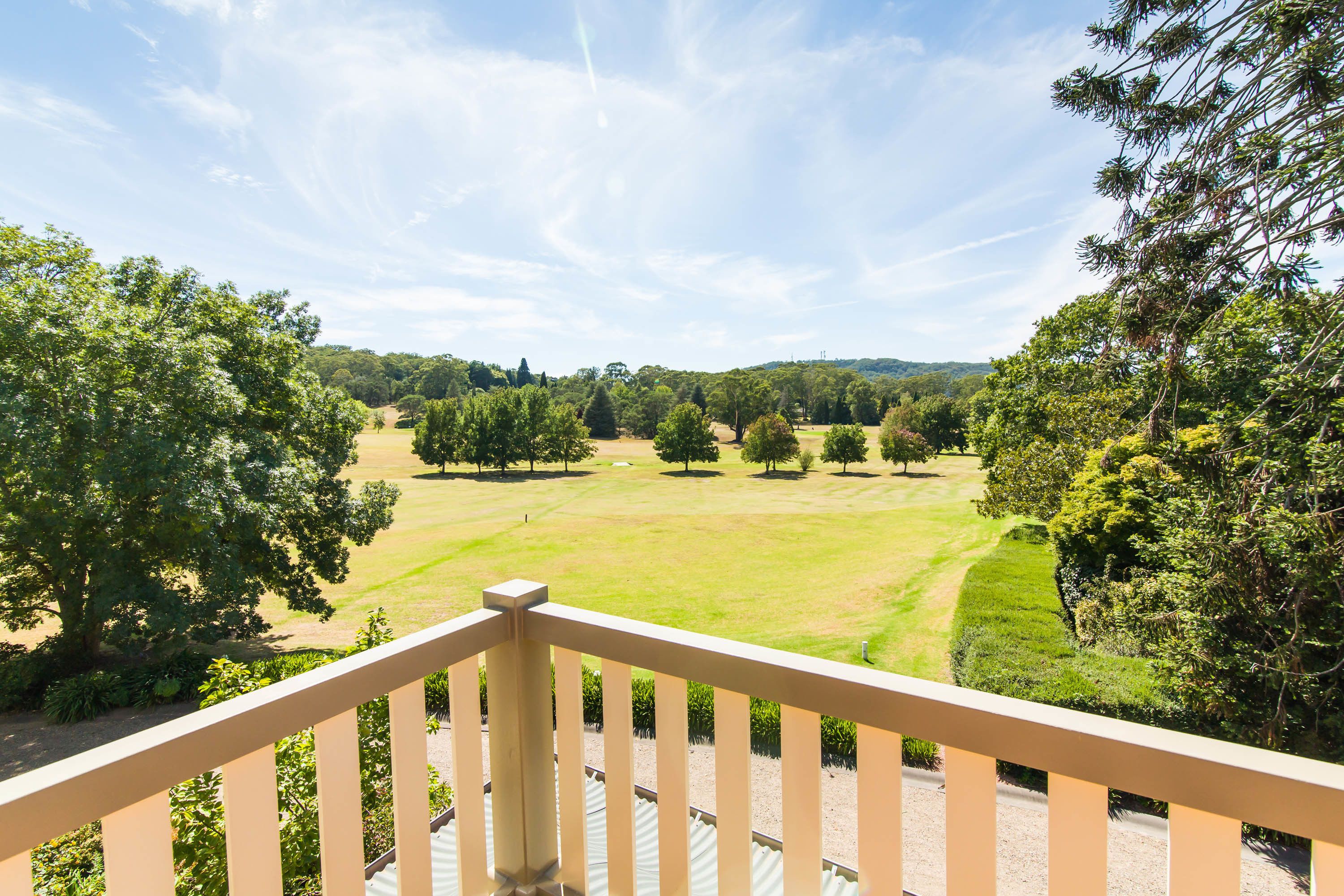 Un balcón con vistas a un césped cuidado y árboles.