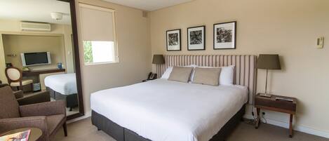 A hotel room with a large bed, a chair, a desk, and a mirror.