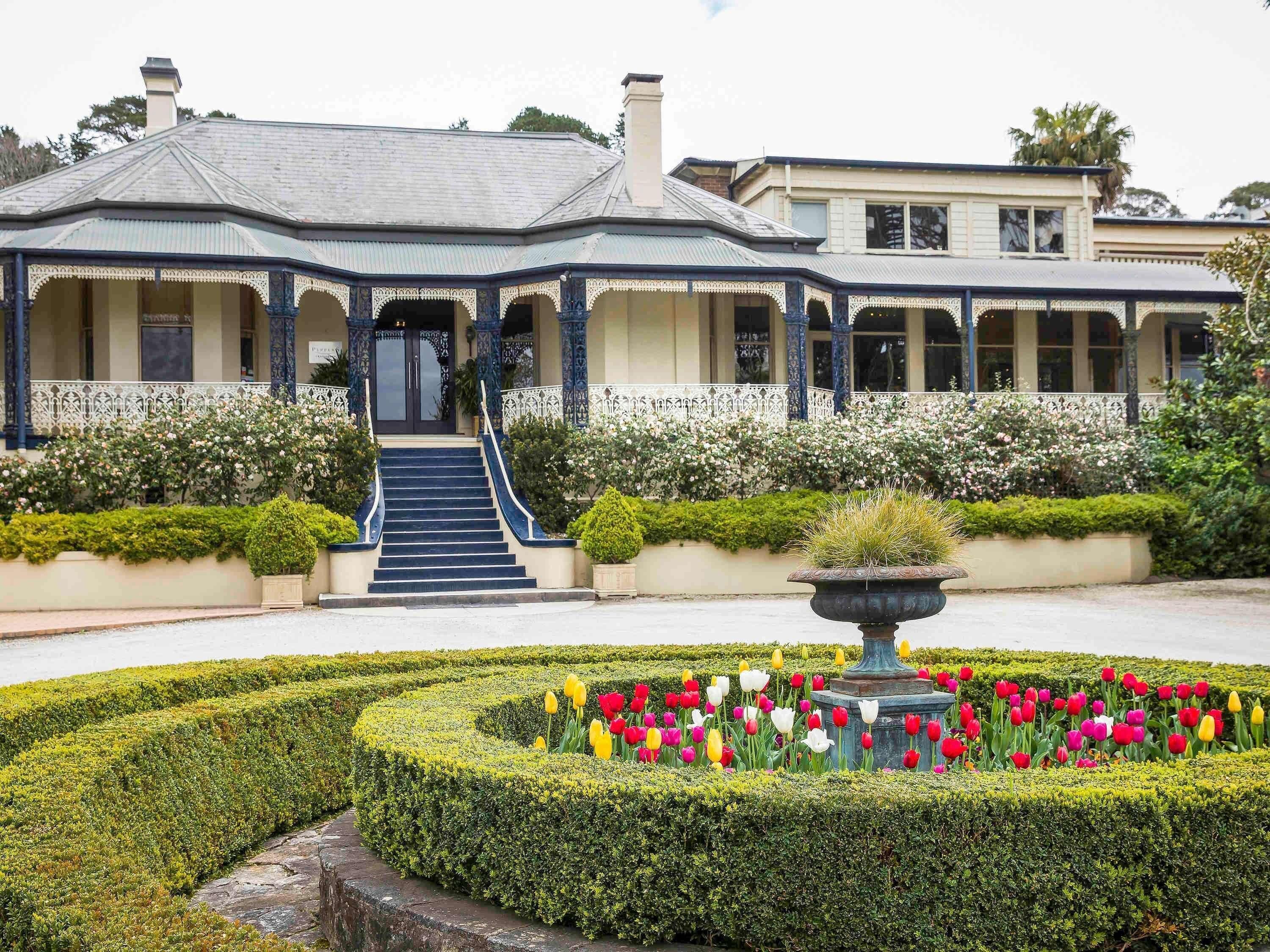 A building with a formal entrance, a garden with a variety of flowers, and a well-maintained lawn.