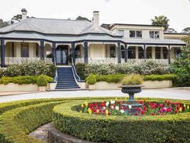 A building with a formal entrance, a garden with a variety of flowers, and a well-maintained lawn.