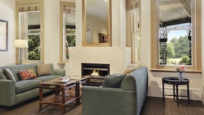 A living room with a sofa, armchair, coffee table, fireplace, and large windows with decorative ironwork. - Peppers Craigieburn (Bowral)